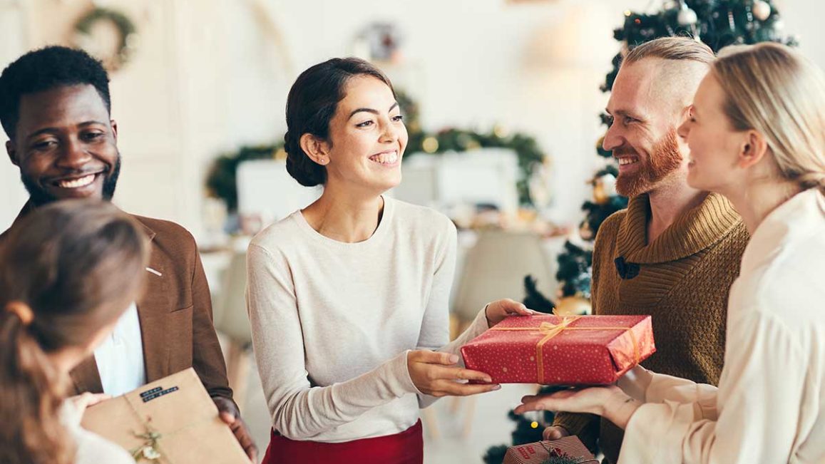 a woman hands a gift to her friend while spending the sober holidays with a group of her friends