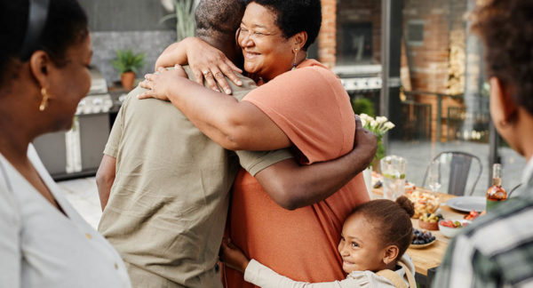 a woman smiles while hugging a man and a young child hugs the woman hugging the man showing a family recovering together