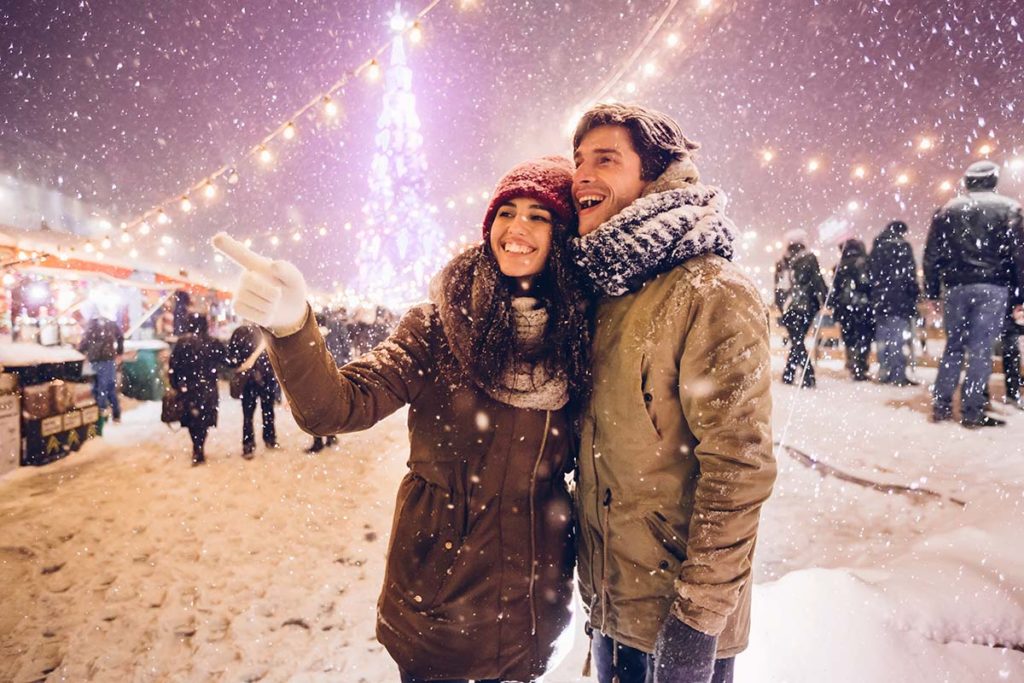 a couple stands outside in front of a lighted christmas tree in the snow while understanding the importance of mental health during holidays