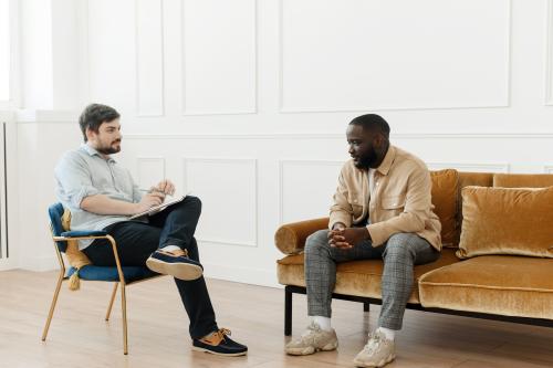 a counselor sits in a chair while talking to a man sitting on the couch and in his cocaine addiction treatment program