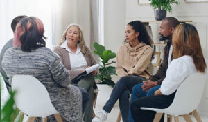 a family sits around in chairs in a circle with a therapist discussing their concerns in their alumni and family therapy program