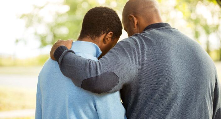 an adult son is hugged by his father after discussing the effects of an alcoholic parents on children