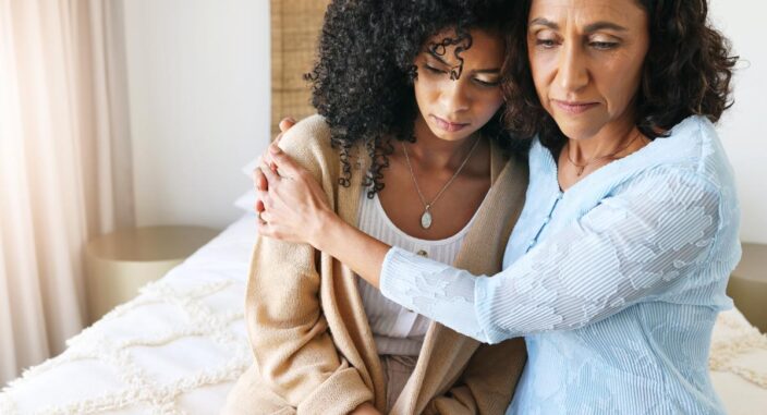 an older woman hugs adult woman wondering to herself about how to help an alcoholic family member