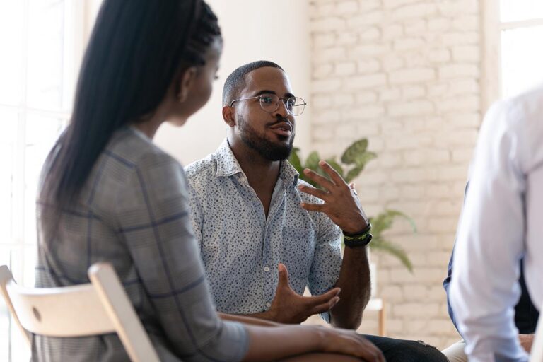 a man sits and talks with group members who are listening to him talk about the benefits of outpatient detox