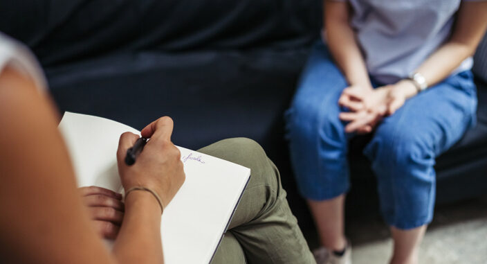 a specialist sits with a notepad in her lap and takes notes about the health risks of bulimia nervosa and discusses those with the patient sitting across from her