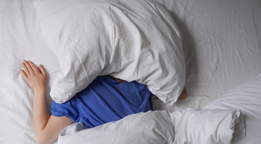 person in bed in sleep-friendly environment with pillow over their head