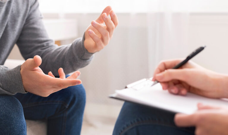 a patient talks with their hands and asks their therapist what is food trauma while their therapist takes notes on a clipboard