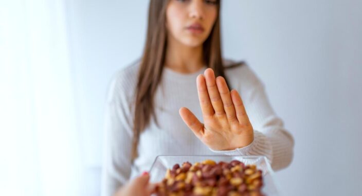 woman holds her hand to a plate of peanuts waving them off after she wonders what is pica