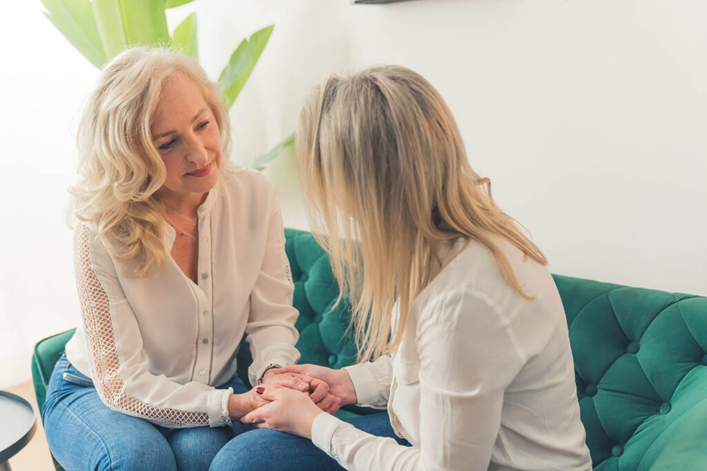 two women sit on a couch together and are discussing how to help a depressed partner