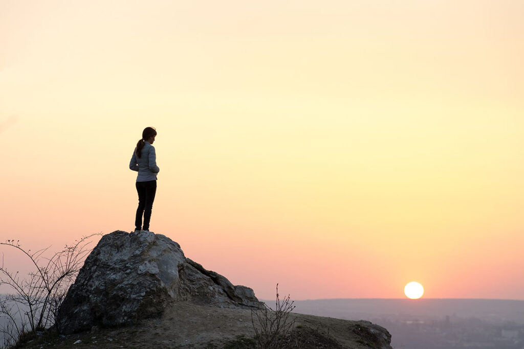 a person stands on a rock near water during sunset and thinks about the connection between loneliness and addiction
