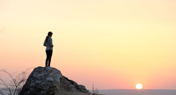 a person stands on a rock near water during sunset and thinks about the connection between loneliness and addiction