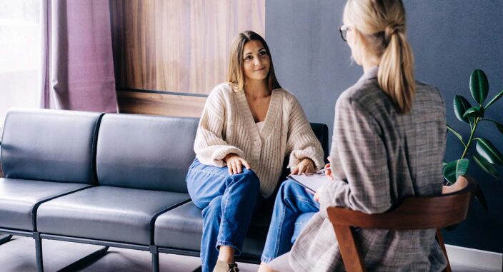 a woman patient sits on a couch and talks to her therapist sitting across from her about the benefits of mat for alcohol use disorder