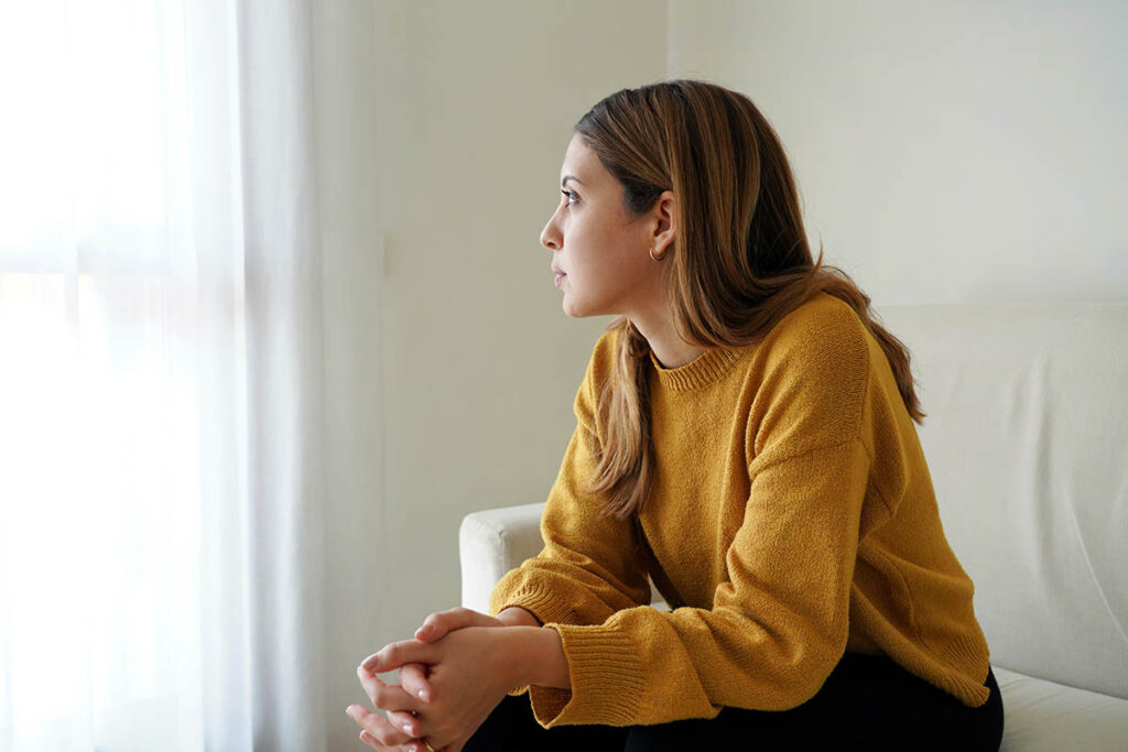 a woman sits in a chair and looks out the window thinking about the connection between depression and eating disorders