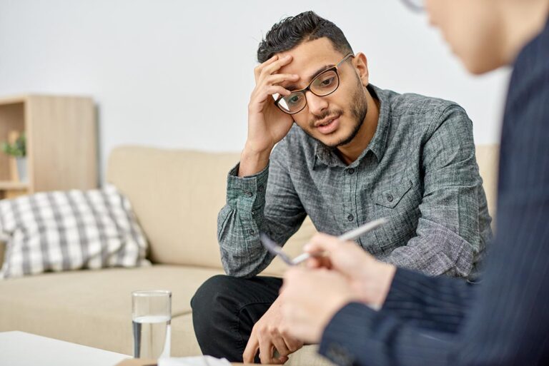 man with glasses holds his head while he listens to his therapist explain substance-induced anxiety disorder