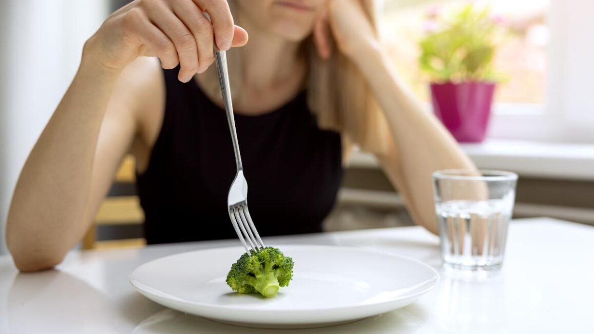 a person holds a fork to a piece of broccoli on their plate thinking about the signs of eating disorder relapse