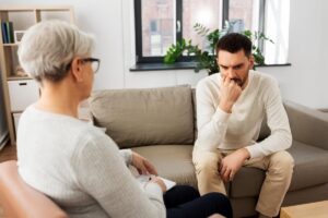 a concerned man sits on a couch discussing his depression symptoms to therapist in depression treatment 