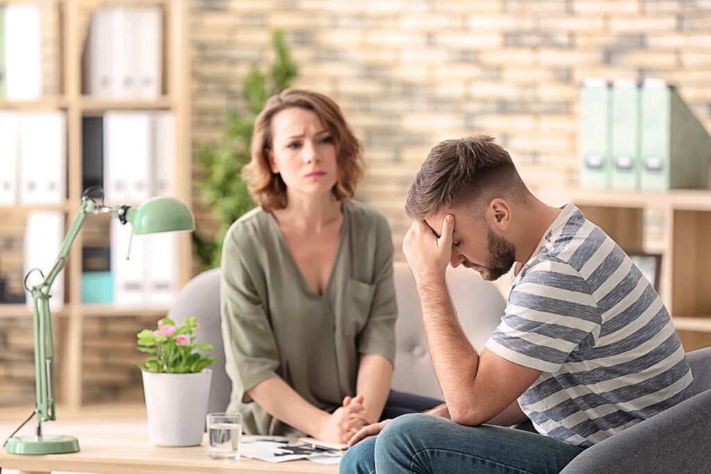 a woman sits with an upset men while woman helps hime with understanding the levels of behavioral health care