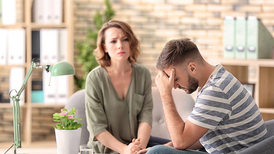 a woman sits with an upset men while woman helps hime with understanding the levels of behavioral health care